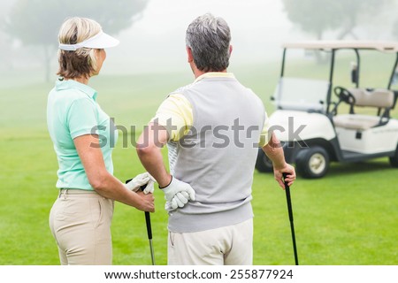 Happy golfing couple with golf buggy behind on a foggy day at the golf course