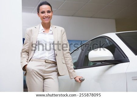 Smiling businesswoman holding a car door handles at new car showroom