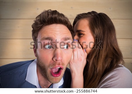 Woman whispering secret into friends ear against bleached wooden planks background