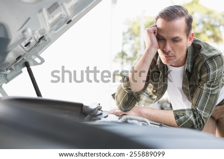 Upset man checking his car engine after breaking down in a car park