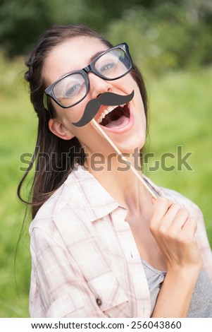 Pretty brunette smiling at camera with fake mustache on a sunny day