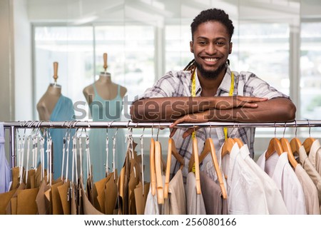 Portrait of male fashion designer leaning on rack of clothes