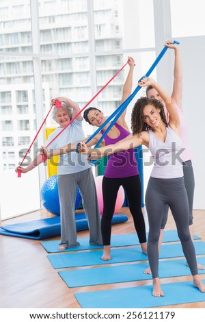 Full length portrait of happy female friends exercising with resistance bands in gym