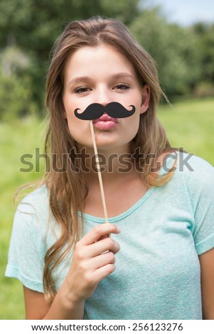 Pretty blonde smiling at camera with fake mustache on a sunny day
