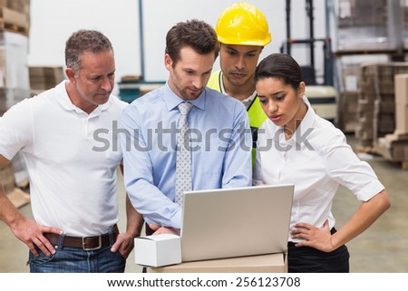 Warehouse managers and worker looking at laptop in a large warehouse