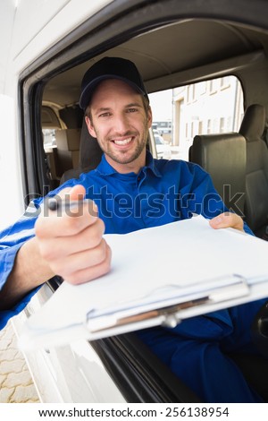 Happy delivery man showing clipboard to sign to customer outside the warehouse