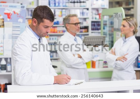 Pharmacist in lab coat writing a prescription in the pharmacy