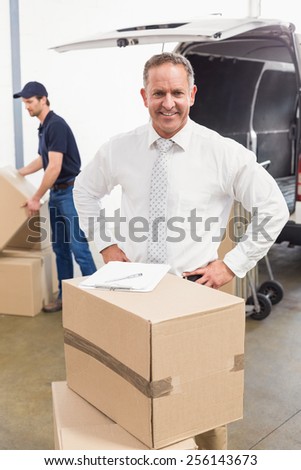 Smiling manager standing behind stack of cardboard boxes in a large warehouse