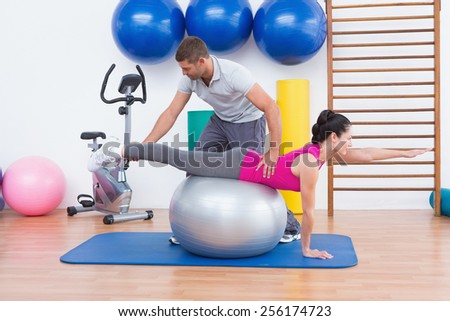 Trainer with woman on exercise ball in fitness studio