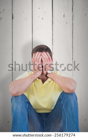Casual man with head in hands against white wood