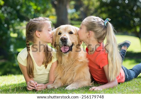 Sisters kissing their dog in the park on a sunny day