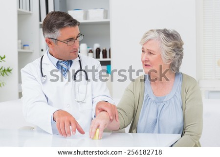 Male doctor assisting female patient to hold weight at table in clinic