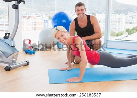 Blonde woman working on exercise mat with her trainer in fitness studio