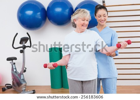 Therapist helping senior woman fit dumbbells in fitness studio