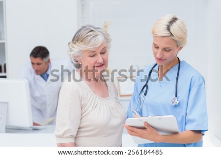 Nurse communicating with female patient while doctor using computer in background at clinic