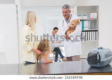 Veterinarian holding cat with its owners in medical office