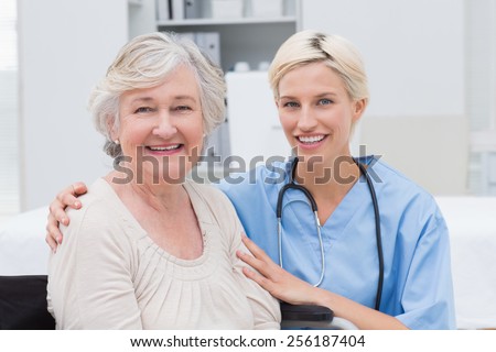 Portrait of friendly nurse with arm around senior patient in clinic