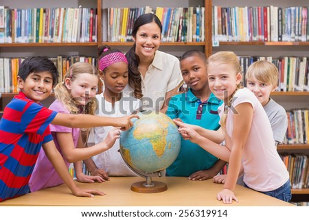 Cute pupils and teacher looking at globe in library at the elementary school