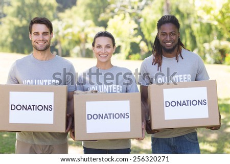Happy volunteers with donation boxes in park on a sunny day