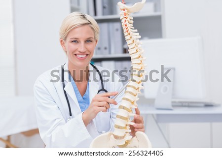 Portrait of confident orthopedic female doctor with anatomical spine in clinic