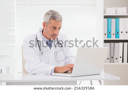 Serious doctor using laptop in medical office