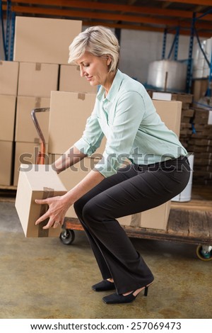 Warehouse manager picking up cardboard box in a large warehouse