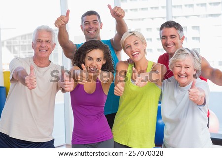 Portrait of happy friends gesturing thumbs up in fitness club