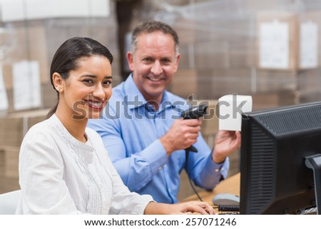 Manager scanning box while his colleague typing on laptop in a large warehouse