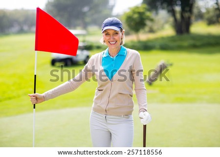 Female golfer smiling at camera and holding her golf club on a sunny day at the golf course