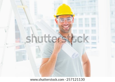 Portrait of smiling handyman holding rolled up blueprint in bright office