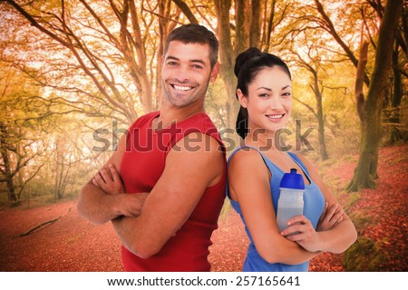Fit man and woman smiling at camera together against peaceful autumn scene in forest