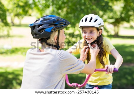 Mother attaching her daughters cycling helmet on a sunny day