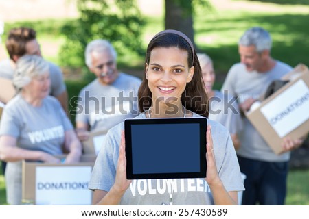 Smiling volunteer brunette showing tablet pc screen on a sunny day