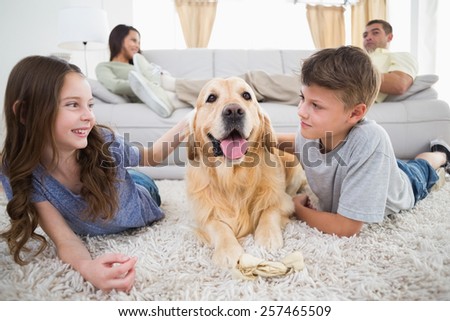 Cute siblings stroking dog on rug while parents relaxing on sofa at home