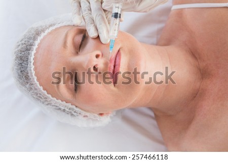 Woman receiving botox injection on her lips in medical office