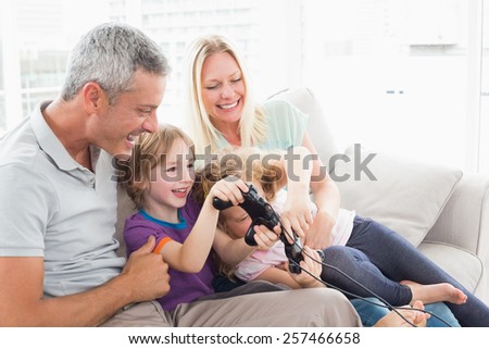 Happy parents looking at children playing video game while sitting on sofa at home