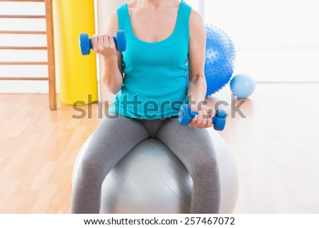 Woman exercising with dumbbells on fitness ball in fitness studio