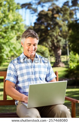 Man sitting on park bench using laptop on a sunny day