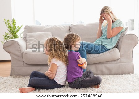 Angry siblings sitting arms crossed with upset mother on sofa at home