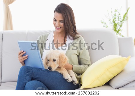Happy beautiful woman with dog using digital tablet on sofa at home