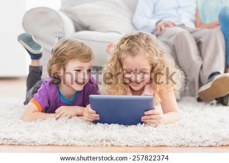 Happy brother and sister using digital tablet while lying on rug at home