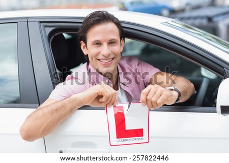 Learner driver smiling and tearing l plate in his car