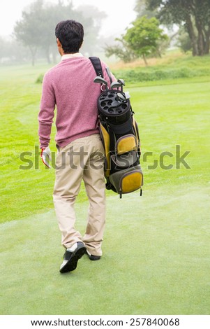 Golfer walking away holding golf bag at golf course