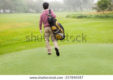 Golfer walking away holding golf bag at golf course