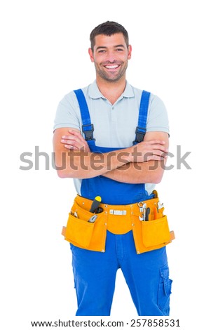 Portrait of happy repairman in overalls wearing tool belt standing arms crossed on white background