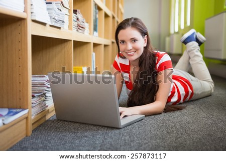 Student using laptop lying on library floor at the university