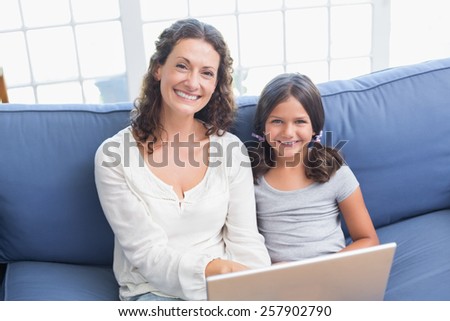 Happy mother and daughter sitting on the couch and using laptop in the living room