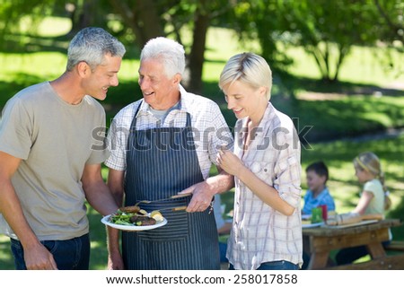 Happy couple with grandfather doing barbecue on a sunny day