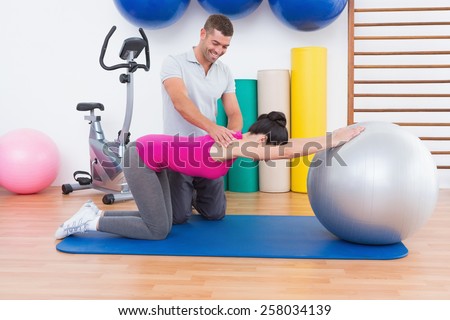 Trainer with woman on exercise ball in fitness studio