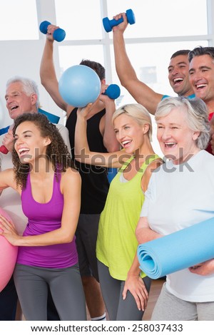 Cheerful friends with hands raised holding equipment in fitness studio